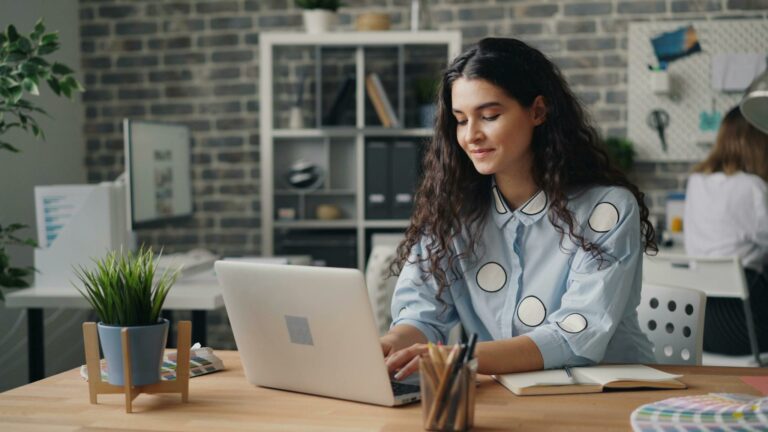 A woman is smiling while working on her laptop